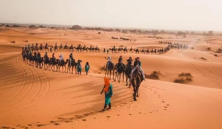 A couple enjoying a romantic camel ride through the stunning Sahara Desert at sunset, capturing the essence of romantic Morocco with golden sand dunes and vibrant sky.